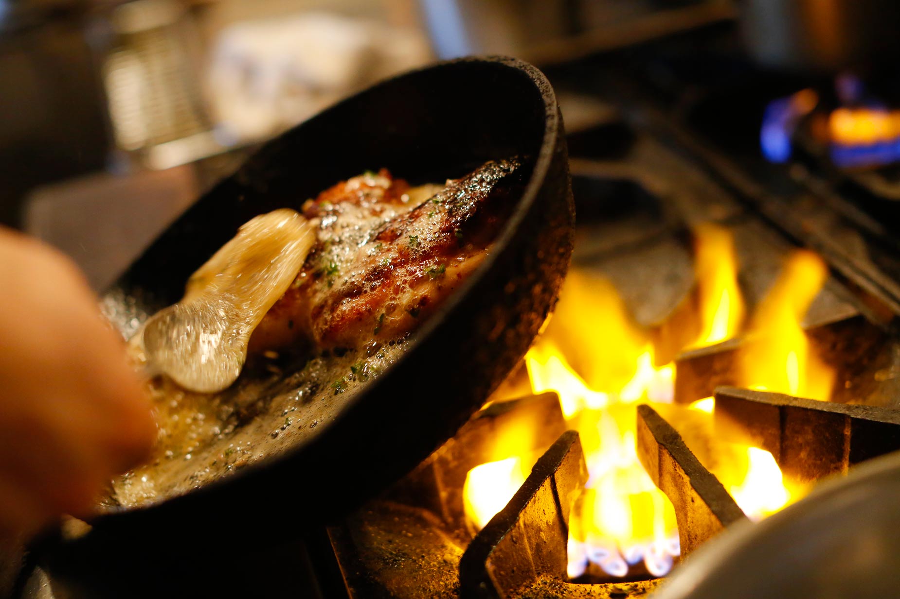 A pan in motion cooks on open flame in restaurant